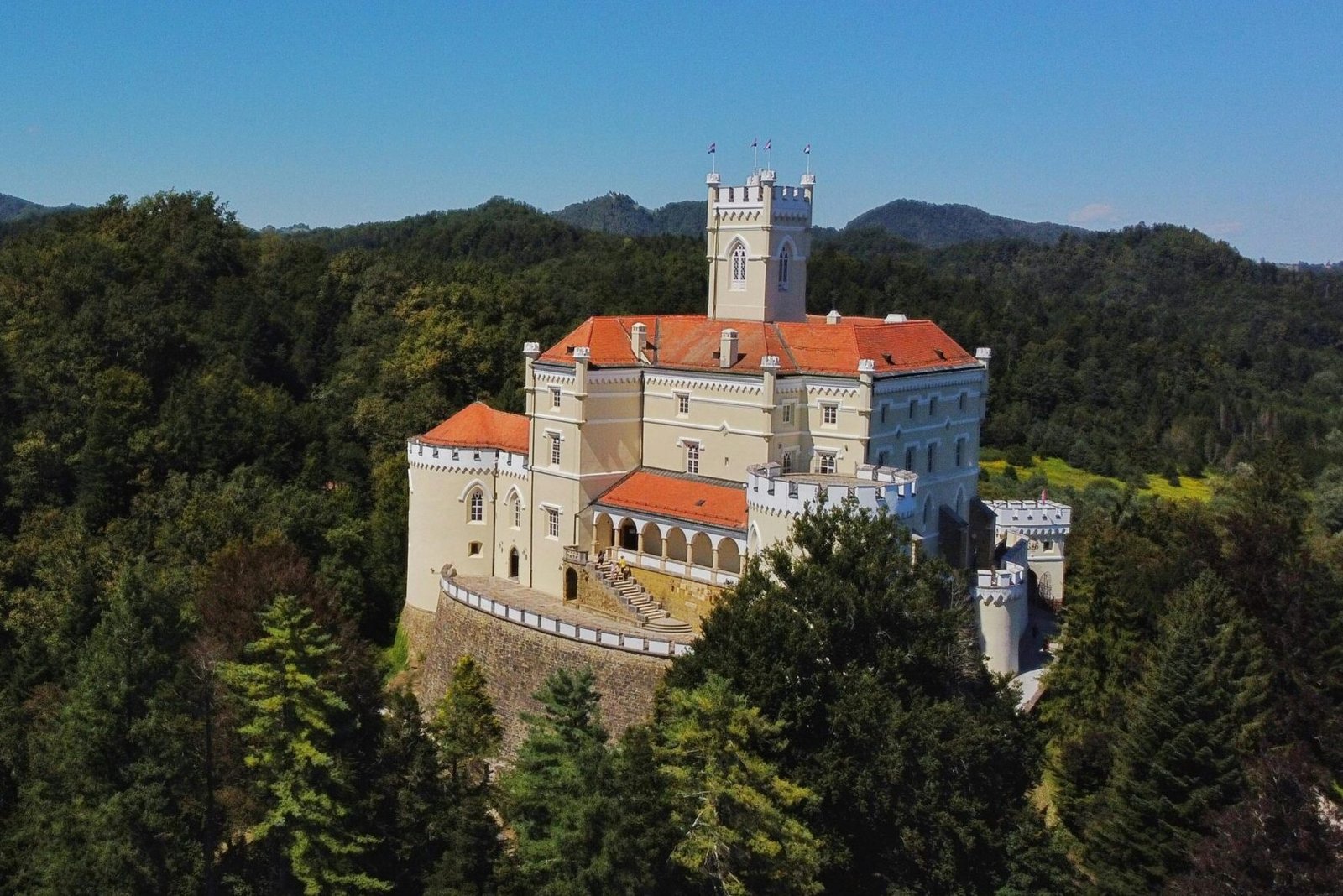 Trakošćan Castle surrounded by lush greenery and a serene lake, set against a clear blue sky
